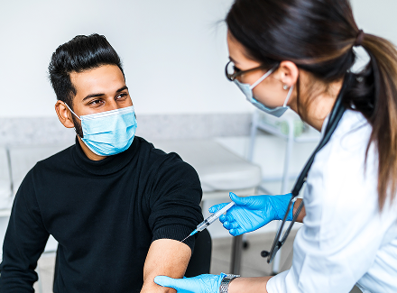 happy-patient-protective-mask-vaccination-male-indian-female-doctor-vaccinating-patient 1
